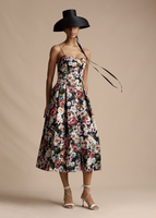 An image of a model wearing the Rickie Dress in Printed Duchess, paired with the Taiko Hat in Black.