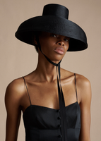 A close up of a model wearing the Rickie Dress in Satin Suiting, paired with the Taiko Hat in Black.