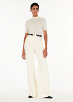 Model wearing the deeda pant in silk wool with the mockneck in ivory and double rose flower belt