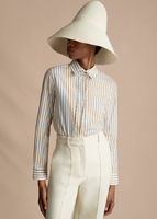 A close up of a model wearing the Shirt with Thin Bow in Stripe Shirting, paired with the Deeda Pant in Silk Wool and Cleo Hat.