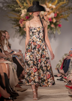 A model facing forward walking down the runway in the Spring 2024 show, wearing the Rickie Dress in Printed Duchess paired with the Taiko Hat in black.