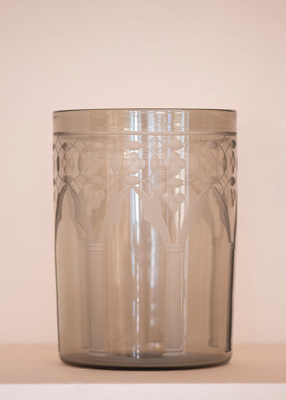 A picture of an engraved, grey, glass vase on a beige background.