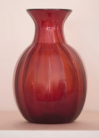 An amber glass vase on a pale pink background. 