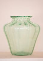 An iridescent green glass vase on a pale pink background. 