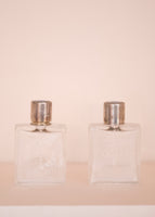 Small glass perfume bottles with blue enamel tops on a pale pink background. 