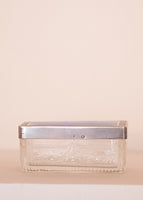 A rectangular dish with a silver top on a pale pink background. 