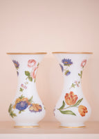 A pair of floral glass vases on a pale pink background. 