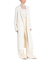 A side angle of a model wearing an all white outfit with an ivory zibeline cashmere coat.