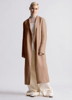 A model wearing a camel colored coat over an ivory lace turtleneck and ivory silk wool pants.
