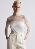A model wearing a Chantilly lace top tucked into a pair of ivory trousers.