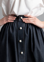 A close up detail shot of a denim skirt with pearl buttons.