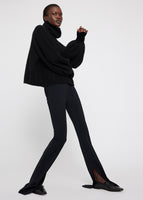 A model wearing a black turtleneck and black slit leg pants.