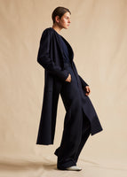 A side-view campaign image of a model in a navy cashmere coat. 