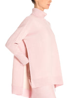 A model wearing a pink sweater with a slit in the side.