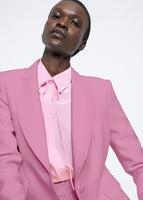 A model wearing a pink suit with a tie neck.