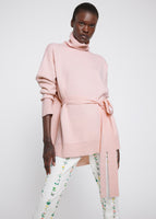 A model wearing a tied, pink turtleneck over a pair of floral cigarette pants. 