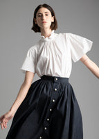 A model wearing a white poplin shirt and indigo denim skirt with pearl buttons.